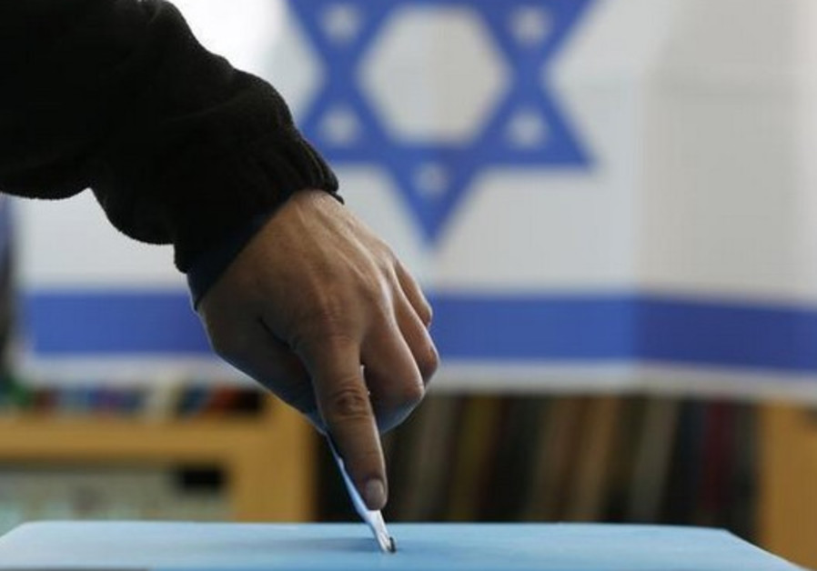 An Israeli flag is seen in the background as a man casts his ballot for the parliamentary election Photo By: REUTERS Israeli elections