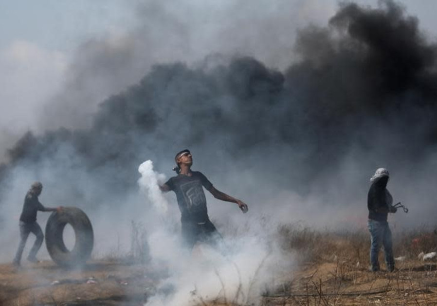 A demonstrator hurls back a tear gas canister fired by Israeli troops during clashes at a Gaza border protest , April 27, 2018 Photo By: REUTERS/IBRAHEEM ABU MUSTAFA Dozens try to breach fence during sixth consecutive week of Gaza protests