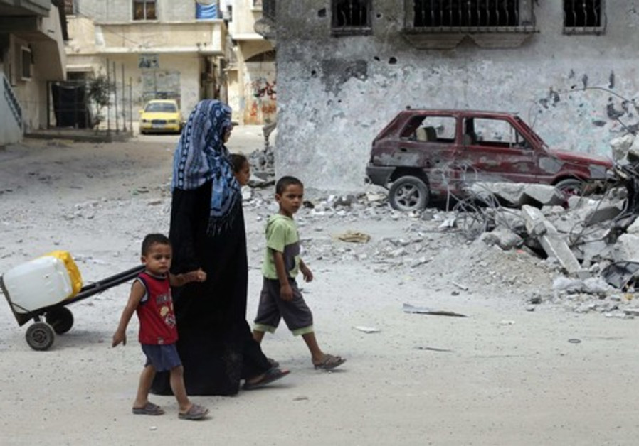 Palestinians walk past a damaged car as they return to their house after filling containers with water from a public tap in Rafah in the southern Gaza Strip Photo By: REUTERS Gaza