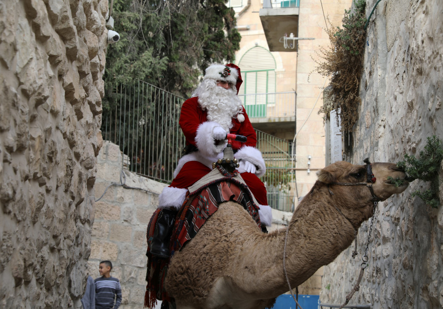 Issa Kassissieh, wearing a Santa Claus costume, rides a camel and distributes Christmas trees in Jerusalem's Old City December 21, 2017 Photo By: AMMAR AWAD/REUTERS Issa Kassissieh, wearing a Santa Claus costume, rides a camel and distributes Christmas trees in Je