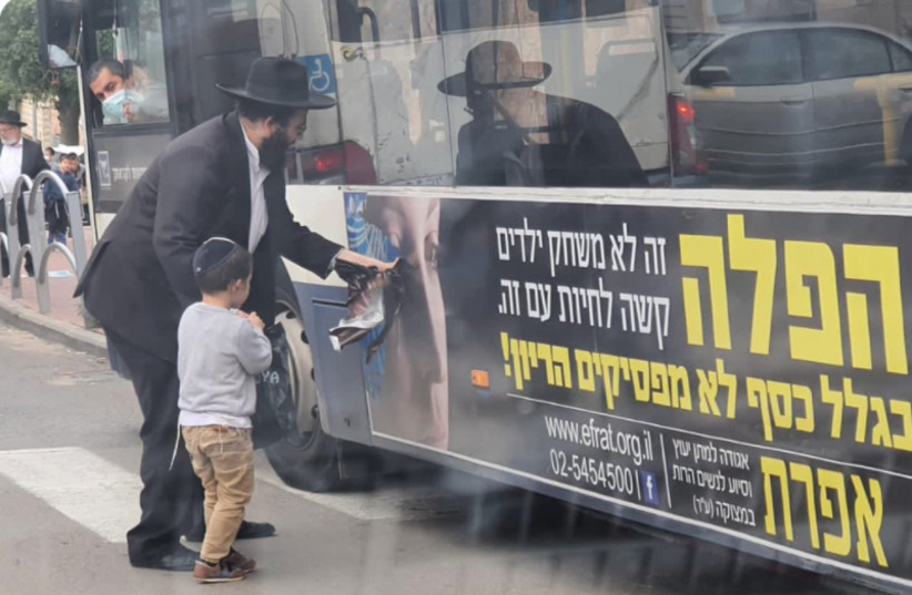 A father shows his son how to pull a woman's face off an anti-abortion organization's bus ad (credit: ISRAEL COHEN ON TWITTER) A father shows his son how to pull a woman's face off an anti-abortion organization's bus ad (credit: ISRAEL COHEN ON TWITTER)