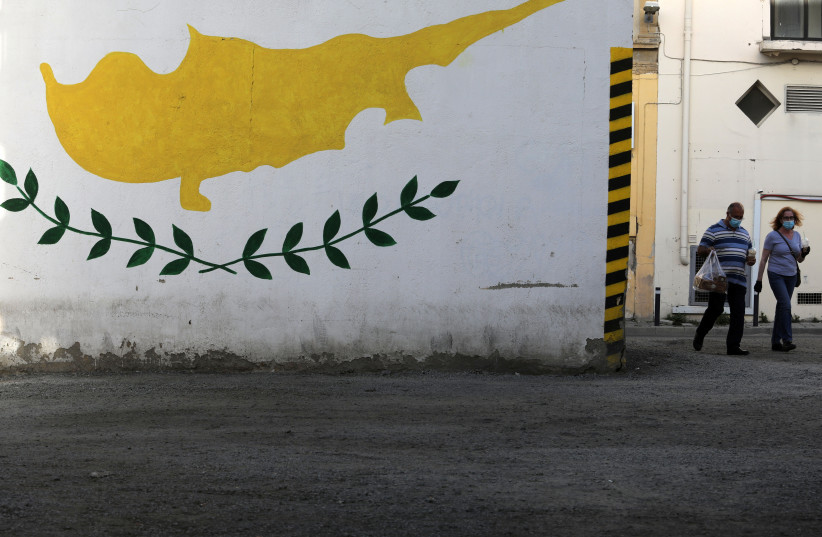 People wearing protective masks walk next to a Cypriot flag painted on a wall in capital Nicosia, Cyprus (credit: YIANNIS KOURTOGLOU/REUTERS) People wearing protective masks walk next to a Cypriot flag painted on a wall in capital Nicosia, Cyprus (credit: YIANNIS KOURTOGLOU/REUTERS)