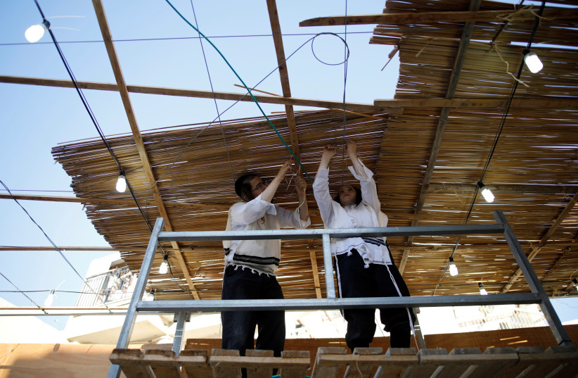 Ultra-Orthodox Jewish men build a ritual booth, known as a sukkah, used during the Jewish holiday of Sukkot, in Ashdod, Israel September 20, 2018. (credit: REUTERS/AMIR COHEN) Ultra-Orthodox Jewish men build a ritual booth, known as a sukkah, used during the Jewish holiday of Sukkot, in Ashdod, Israel September 20, 2018. (credit: REUTERS/AMIR COHEN)