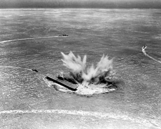 Diorama by Norman Bel Geddes depicting the explosion of depth charges from USS Hammann as she sank alongside USS Yorktown during the afternoon of June 6, 1942. Both ships were torpedoed by a Japanese submarine while Hammann was assisting with the salvage of Yorktown. USS Vireo (AT-144) is shown at left, coming back to pick up survivors, as destroyers head off to search for the submarine. Photo by the U.S. Navy, courtesy of the National Archives.